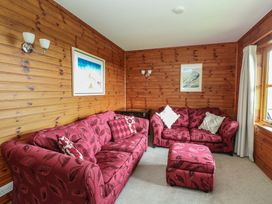 A living room with two red patterned sofas a matching ottoman wooden paneled walls and framed pictures at Creag Mhor Lodge Back of Keppoch near Arisaig