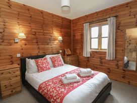 A bedroom with a double bed with white and red bedding two wooden bedside dressers wall lamps a window with curtains and a mirror on the wall at Creag Mhor Lodge Back of Keppoch near Arisaig