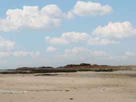 A sandy beach with rocks and grassy areas under a blue sky with scattered clouds at Creag Mhor Lodge Back of Keppoch near Arisaig