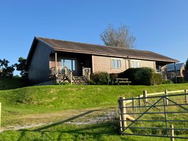A single-story wooden house with steps leading to two entrances and outdoor seating on a grassy hill at Creag Mhor Lodge Back of Keppoch near Arisaig