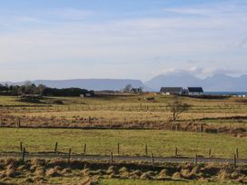 A rural landscape with fenced fields, houses, cows, a road, and mountains in the background at Glen Mhor Lodge in Arisaig