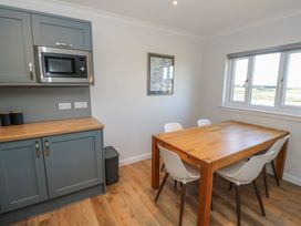 A dining area with wooden table and white chairs next to kitchen cabinets with microwave at Glen Mhor Lodge in Arisaig