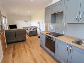 An open-plan kitchen and living area with blue cabinets a wooden countertop gray sofas a wooden floor and a television at Glen Mhor Lodge in Arisaig