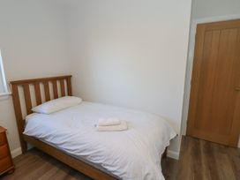 A bedroom with a wooden single bed a pillow folded towels a wooden bedside table a wooden door and white walls at Glen Mhor Lodge in Arisaig