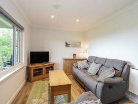 A living room with a gray sofa wooden coffee table TV on wooden stand and a window at Glen Mhor Lodge in Arisaig