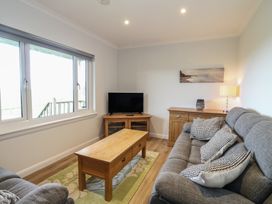 A living room with grey sofas a wooden coffee table a TV on a wooden stand and a sideboard with a lamp at Glen Mhor Lodge in Arisaig
