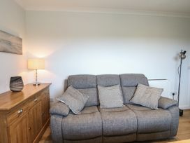 A gray sofa with patterned pillows beside a wooden sideboard with a lamp and decorative vase at Glen Mhor Lodge in Arisaig