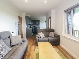 A living area with two grey sofas a wooden coffee table and a view into a kitchen with grey cabinets at Glen Mhor Lodge in Arisaig