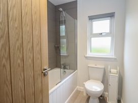 A bathroom with a bathtub and shower a toilet a window and a wooden door at Glen Mhor Lodge in Arisaig