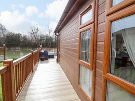 A wooden deck with railing and seating area overlooking a lake at The Lake House in Marston near Barkston