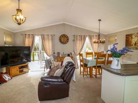 An open living and dining area with a leather sofa wooden dining table tv and flowers on a counter at The Lake House in Marston near Barkston