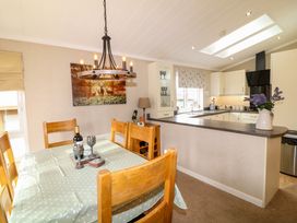 A dining room with a wooden table and chairs next to a kitchen with white cabinets and a black stove at The Lake House in Marston near Barkston