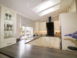 A kitchen with white cabinets a window with a floral blind and glassware displayed at The Lake House in Marston near Barkston