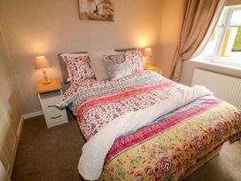 A bedroom with a double bed with patterned bedding two bedside tables with lamps a window and curtains at The Lake House in Marston near Barkston