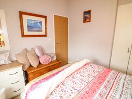 A bedroom with a bed covered by a floral quilt a wooden chest with pillows and blankets a dresser and two framed pictures on the walls at The Lake House in Marston near Barkston