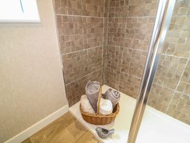 A shower corner with a brown tiled wall a basket with rolled towels and a small bird-shaped container at The Lake House in Marston near Barkston