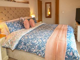 A bedroom with a bed with floral bedding four pillows two pink cushions a pink throw and a wall mirror at The Lake House in Marston near Barkston