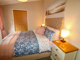 A bedroom with a bed with floral bedding a wooden nightstand with a lamp and doors at The Lake House in Marston near Barkston