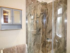 A bathroom with a glass shower enclosure a gray wall-mounted cabinet and towels on a radiator at The Lake House in Marston near Barkston