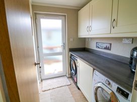 A laundry room with a washer and dryer under a countertop and storage cabinets above at The Lake House in Marston near Barkston