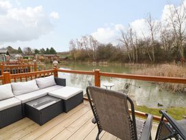 An outdoor deck with seating overlooking a pond with trees in the background at The Lake House in Marston near Barkston