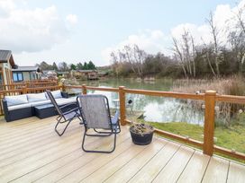 A wooden deck with outdoor seating furniture overlooking a pond with trees at The Lake House in Marston near Barkston