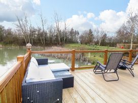 An outdoor deck with a wicker sofa and reclining chairs overlooking a pond and trees at The Lake House in Marston near Barkston