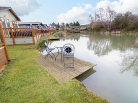 A lakeside view with chairs and a table on a wooden deck near homes at The Lake House in Marston near Barkston