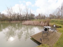 A small wooden dock with two metal chairs and a table by a pond surrounded by trees and reeds at The Lake House in Marston near Barkston
