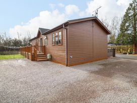 A brown wooden house with a raised deck and stairs surrounded by gravel and lawn at The Lake House in Marston near Barkston