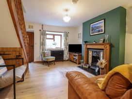 A living room with a brown leather sofa a green accent wall with a fireplace and a television on a wooden stand at Gwynfa in Ysbyty Ifan