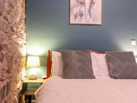 A bed with two large pillows and white bedding a bedside table with a lamp and a stone wall on the left at Gwynfa in Ysbyty Ifan