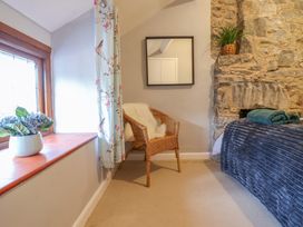 A corner of a bedroom with a wicker chair, a bed with a blanket and towels, a stone wall, a window with a flowerpot, and a square mirror on the wall at Gwynfa in Ysbyty Ifan