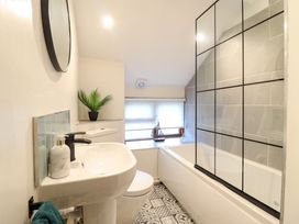A bathroom with a sink, toilet, bathtub with a glass panel, patterned floor tiles, and a window with blinds at Gwynfa in Ysbyty Ifan