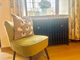 A green chair with a cushion featuring sheep beside a black radiator under a window with floral curtains at Gwynfa in Ysbyty Ifan