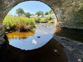 A view of a river under a stone bridge with grass and houses at Gwynfa Ysbyty Ifan
