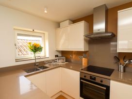 A kitchen with a sink under a window with flowers a toaster a knife block an oven and stovetop at Apartment 1 in Scarborough