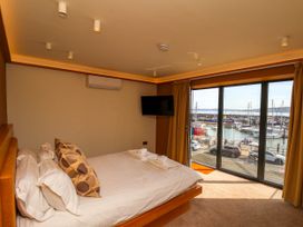 A bedroom with a bed and pillows next to large windows overlooking a harbor at Apartment 1 in Scarborough