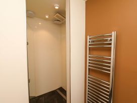 A bathroom with a walk in shower with a rain showerhead and a stainless steel towel rack on an orange wall at Apartment 1 in Scarborough