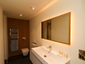 A bathroom with a wall-mounted toilet towel rack a large mirror and a sink with toiletries at Apartment 1 in Scarborough