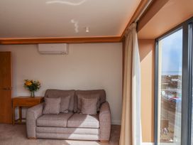 A small sofa with cushions next to a side table with flowers and a large window at Apartment 2 in Scarborough