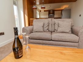 A gray sofa with cushions in front of a kitchen with a wooden dining table and hanging lights with a bottle and two glasses on a wooden coffee table at Apartment 2 in Scarborough