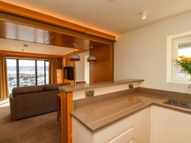 A kitchen with countertop and sink adjacent to a living room with sofa and large window overlooking boats at Apartment 2 in Scarborough