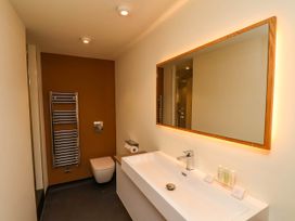 A bathroom with a wall-mounted toilet a towel rack a large rectangular mirror and a long white sink with toiletries at Apartment 2 in Scarborough