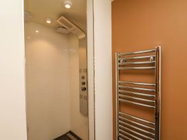A shower area with white tiled walls and a ceiling rain showerhead next to a chrome towel radiator on a brown wall at Apartment 2 in Scarborough