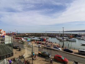 View of a harbor with boats docked and people walking along the waterfront near parked cars at Apartment 2 in Scarborough