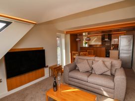 A living room with a grey sofa and wooden coffee table facing a wall-mounted TV and an open kitchen with a dining table at Apartment 3 in Scarborough