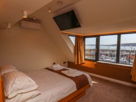 A bedroom with a bed and a wall mounted television next to a window with a view of boats at Apartment 3 in Scarborough