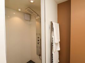 A shower area with a modern shower panel and white tiled walls next to a towel rack with white towels in Apartment 3 Scarborough
