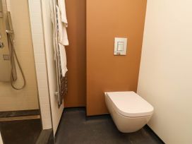 A bathroom with a wall-mounted toilet shower area with a handheld showerhead and a towel rack with white towels at Apartment 3 in Scarborough